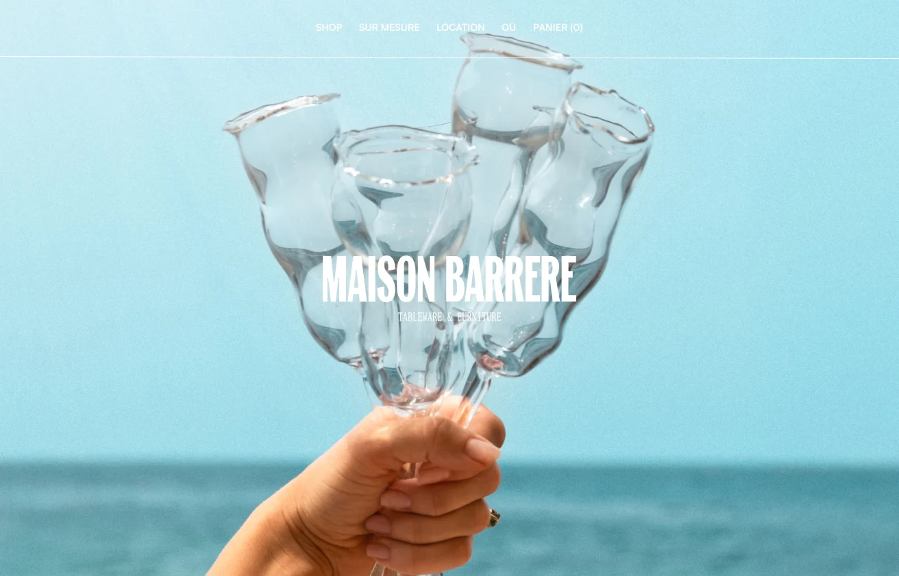 Page d'accueil de Maison Barrère : une pièce de verre soufflé tenue devant la mer.